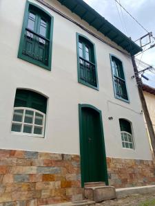 uma casa branca com janelas verdes e uma porta em Casa próxima ao centro de convenções da UFOP em Ouro Preto