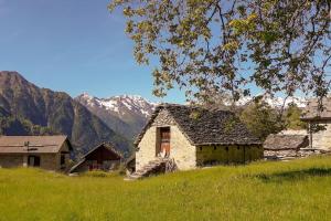 an old house in a field with mountains in the background at Chalet Alpe Quaggiui in Calasca Castiglione