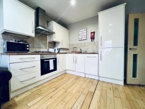 a kitchen with white cabinets and a wooden floor at Lovely 3 Dbl Bed (sleeps upto 6) close to centre. in Manchester