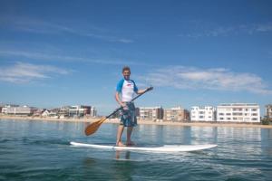 a man standing on a paddle board in the water at Superb Sandbanks Apartment near Beach and Bars with Free Parking in Poole