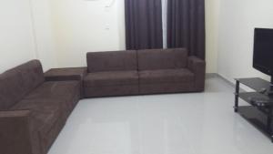 sala de estar con sofá marrón y TV en Golden Seasons Furnished Apartment, en Salalah