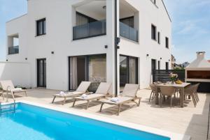 eine Terrasse mit Tisch und Stühlen neben einem Swimmingpool in der Unterkunft Villa Bellatrix 1 & 2 - two heated pools & jacuzzi in Vrsi