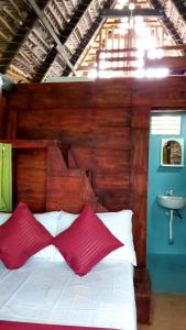 Bett mit roten Kissen und Waschbecken in einem Zimmer in der Unterkunft ULPATHA ECO LODGE in Kurunegala