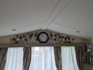 un reloj en un estante en una habitación con ventanas en The Ocean Pearl caravan number 50 situated on the Cove holiday park, en Southwell