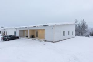 un bâtiment blanc avec une voiture garée dans la neige dans l'établissement Villa Morning Star, à Rovaniemi