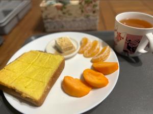 a plate of food with bread and oranges and a cup of tea at 九份 珂菲私旅-知雨樓 附心意早餐 Jiufen Cafe Sleep B&B-Rain House 日夜間導覽 合法民宿 in Jiufen