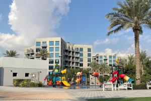 a playground in front of a building with a palm tree at Elite LUX Holiday Homes - Modern One Bedroom Apartment in MAG 5, Dubai South in Dubai