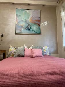a bed with a pink comforter and a painting on the wall at Apartment Bombonjera in Užice