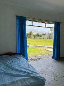 a bedroom with a bed and a window with blue curtains at Casa de Campo en Conache in Trujillo