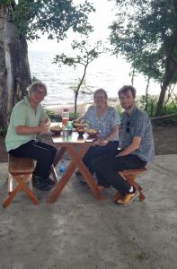 tres personas sentadas en una mesa de picnic cerca del agua en Cabañas piedra grande ometepe, en Altagracia