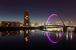 uma ponte com uma luz roxa sobre a água à noite em Archillects - Entire Two Bedroom Luxury House em Glasgow