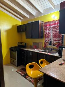 una cocina con paredes amarillas, armarios negros y sillas amarillas en Epic Paradise en Ocho Rios
