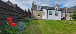 a house with a fence and a yard with flowers at Mike's 3-bedroom Countryside Cottage in Alness