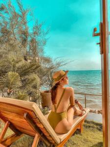 a woman in a green bikini sitting in a chair on the beach at CHILL HOUSE by the beach in Phu Quoc