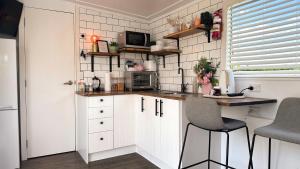 a small kitchen with white cabinets and a table and chairs at Rustling Oaks NZ Tropical Tiny House in Tamahere