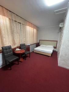 アルマトイにあるZolotoi Drakon Hotelのベッド1台、椅子2脚、テーブルが備わる客室です。