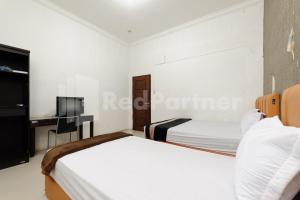 a white bedroom with two beds and a tv at RedDoorz at Wisma Nabila Syariah near Masjid Raya Baiturrahman Banda Aceh in Banda Aceh +13 photos