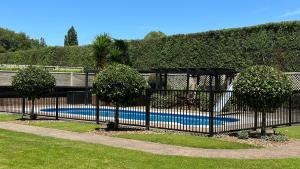 a black fence with trees in front of a pool at Rustling Oaks NZ Boho Pool House in Cambridge
