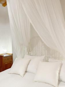 Cama blanca con cortinas y almohadas blancas en Agriturismo "Le Cannelle" spa & day wellness, en Fossombrone