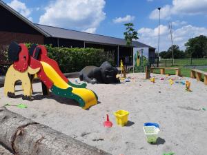 a playground with toys in the sand in front of a building at Camping Nieuw Romalo in Voorthuizen