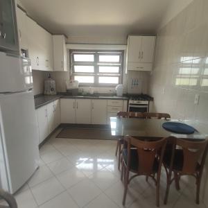 cocina con armarios blancos, mesa y sillas en Casa de 2 Quartos na Praia da Joaquina, en Florianópolis