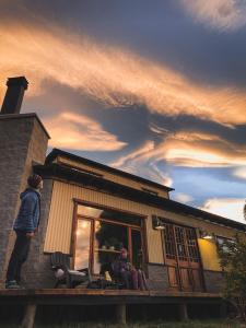 un hombre parado en el porche de una casa con una formación de nubes en Hostel I Keu Ken en El Calafate