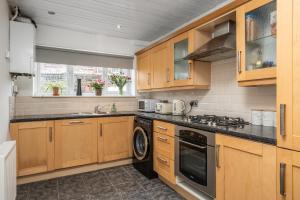 a kitchen with wooden cabinets and a washer and dryer at Comfortable and Peaceful House in St Helens in Thatto Heath
