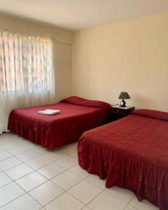 two beds in a room with red sheets and a lamp at Hotel Moderno Coroico in Coroico