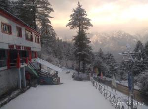 a building in the snow with mountains in the background at Manikarn Resort in Joshīmath