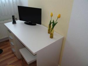 a white desk with a monitor and flowers in a vase at Venner Gasthaus in Ostercappeln