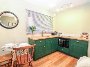 a kitchen with green cabinets and a table with a mirror at Goldcrest Hide in Bungay