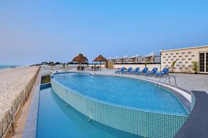 una piscina junto a una playa con sillas azules en The Fern Leo Beach Resort , Madhavpur en Porbandar