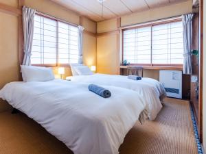 two beds in a room with two windows at Sakurasou Lodge in Nozawa Onsen