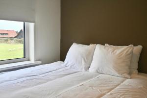 a bed with white pillows in a room with a window at De Viool Appartementen in Buren