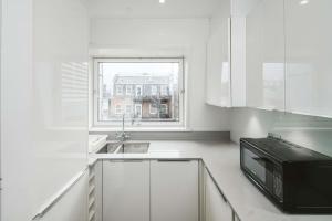a white kitchen with a microwave and a window at Stylish & Peaceful Covent Garden Apartment in London