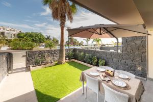 a patio with a table and an umbrella and grass at Relax Golf cerca de la playa in San Miguel de Abona
