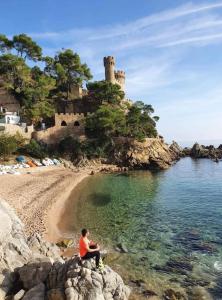 a man sitting on a rock on a beach with a castle at SeaHomes Vacations - ACACIAS Beach&Chic in Lloret de Mar