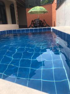 a blue swimming pool with an umbrella and a table at Casa temporada com Piscina in Governador Celso Ramos