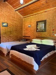1 dormitorio con 1 cama grande en una pared de ladrillo en Pousada Árvore Centenária, en São Thomé das Letras