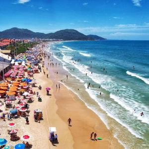 uma praia lotada com muitas pessoas e guarda-sóis em Residencial Marina em Florianópolis