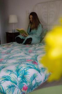 una mujer sentada en una cama leyendo un libro en Quinta Physalis, en Fenais da Luz