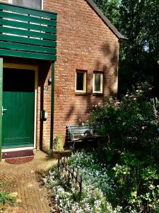 un edificio de ladrillo con una puerta verde y un banco en Blauwe Lelie, en Ewijk