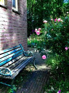 een houten bank naast een bakstenen gebouw met roze bloemen bij Blauwe Lelie in Ewijk