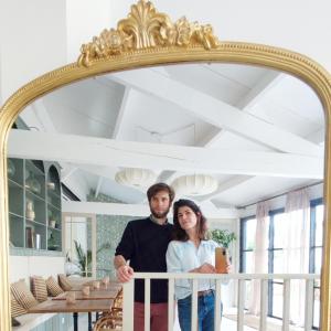 mężczyzna i kobieta stojący przed złotym lustrem w obiekcie Maison Charmeilles - Le studio Canon de Fronsac w mieście Fronsac