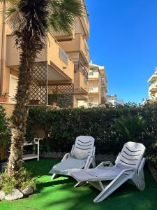 two lounge chairs sitting next to a palm tree in front of a building at Seashell Guest House in Santa Marinella