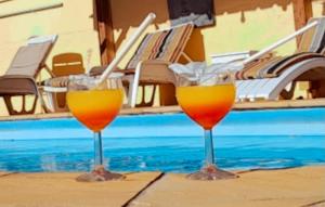 two wine glasses sitting on a table next to a pool at 3 bedrooms villa with city view shared pool and enclosed garden at Pointe aux Piments 1 km away from the beach in Pointe aux Piments