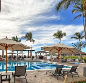 ein Pool mit Stühlen, Sonnenschirmen und Palmen in der Unterkunft Hotel Quijote Inn in Mazatlán