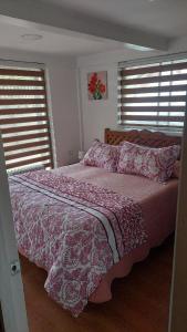una camera da letto con un letto con un piumone rosa e due finestre di Departamentos Buena Vista a El Quisco