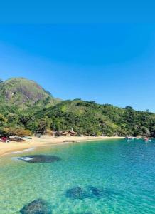 une plage avec de l'eau turquoise et des montagnes en arrière-plan dans l'établissement Pouso da Cajaíba - Chalé Pedaço de Céu, à Parati