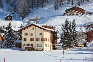 un edificio en la nieve con árboles y montañas cubiertas de nieve en White Pine Lodge Livigno en Livigno